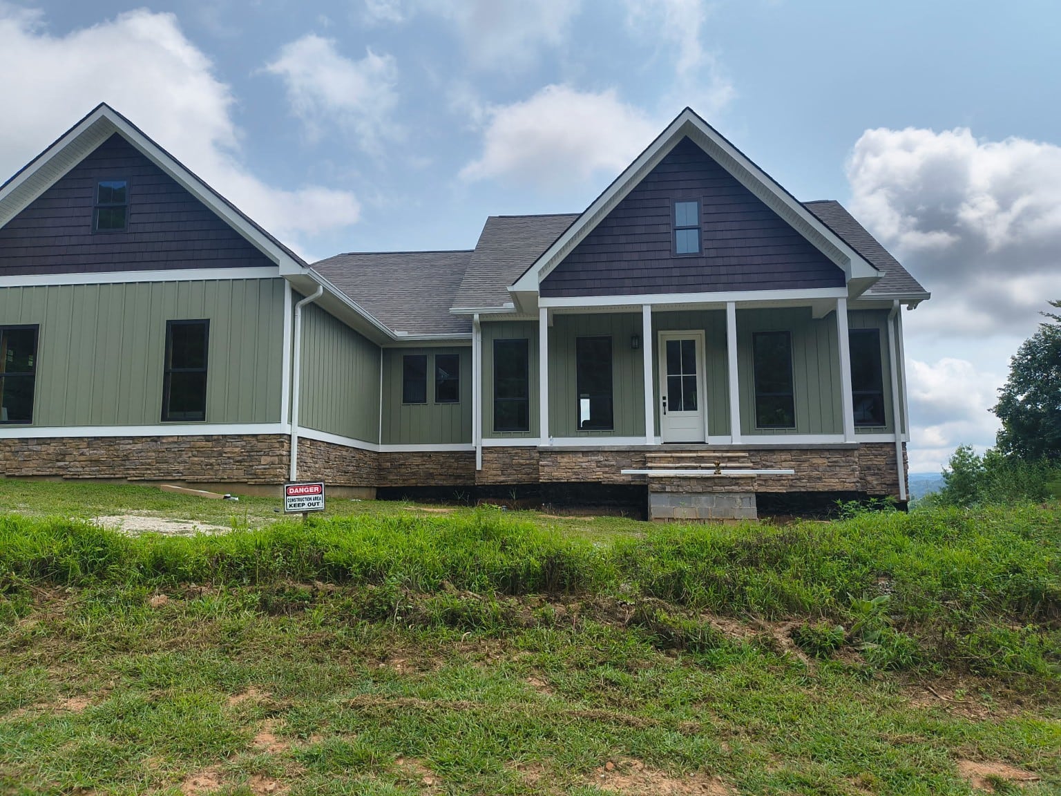 Green-sided home with white gutters and downspouts, dark gables, and a front porch.