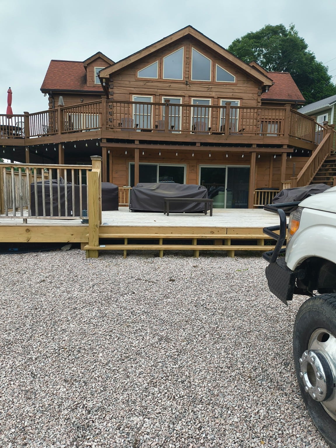 Brown house with red roofs, two levels of decks, and dark gutters along the roof edges.